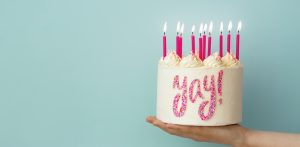 Hand holding birthday cake with pink candles and yay written in sprinkles